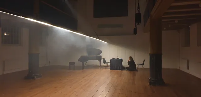 Oblique Time light line spanning a hazy hall above a grand piano